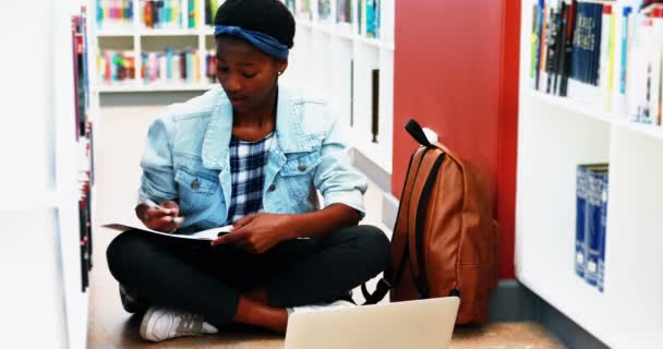 Ragazza della scuola che fa il lavoro a casa durante l'utilizzo di laptop in biblioteca — Video Stock