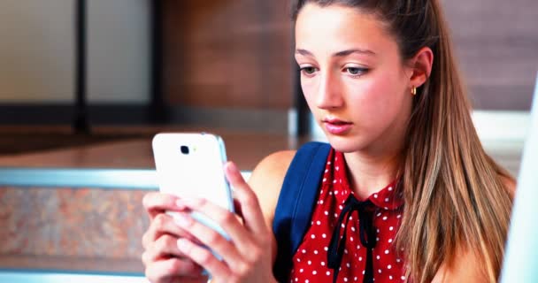 Schoolgirl sitting on staircase and using mobile phone — Stock Video