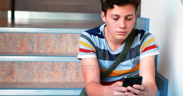 Schoolboy sitting on staircase and using mobile phone — Stock Video