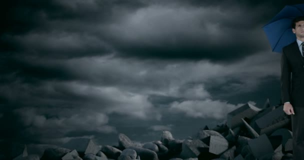 Uomo d'affari con ombrello in piedi su rocce di detriti durante la tempesta — Video Stock