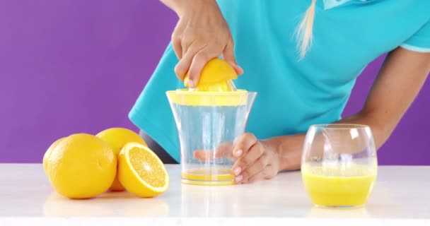 Женщина готовит сладкий сок лайма из соковыжималки на фиолетовом фоне — стоковое видео