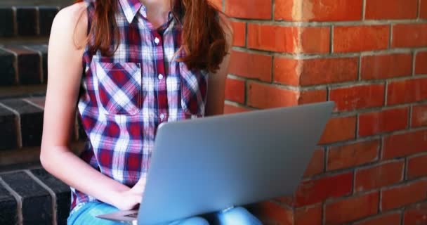 Smiling schoolgirl using laptop on staircase — Stock Video