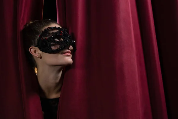 Artista em máscara espreitando através de cortina vermelha — Fotografia de Stock