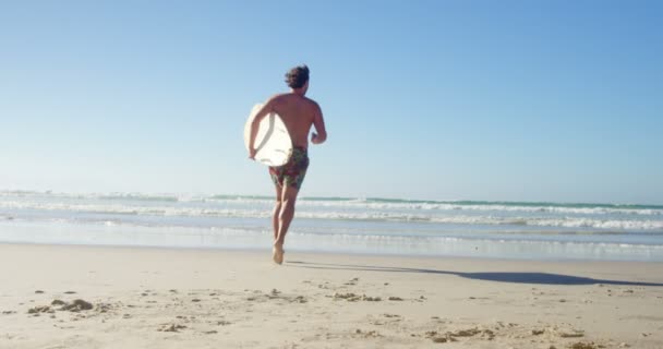 Мужчина бегает с доской для серфинга на пляже в солнечный день — стоковое видео