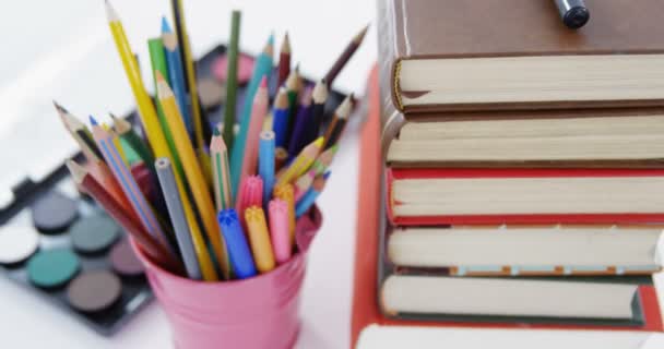 Kleurpotloden in pennenhouder met stapel boeken — Stockvideo