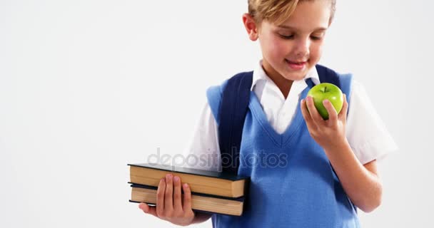Escolar sonriente sosteniendo libros y manzana — Vídeo de stock