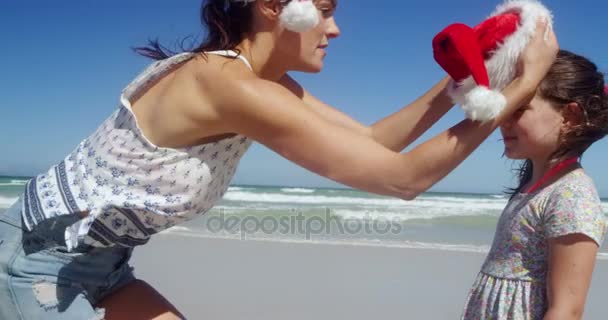 Mother putting santa hat on girl head at beach — Stock Video