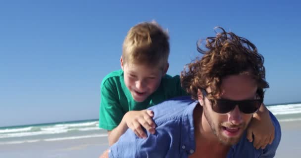 Father giving piggyback ride to his son at beach — Stock Video