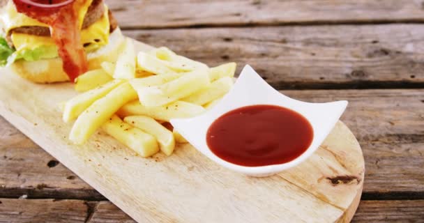 Hambúrguer e batatas fritas com molho de tomate mantidos na tábua de corte — Vídeo de Stock