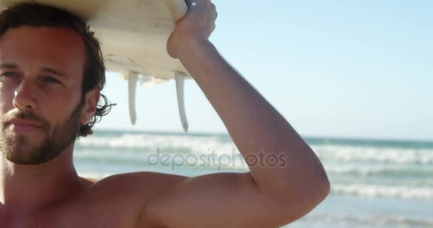 Joven llevando tabla de surf en la cabeza en la playa — Vídeos de Stock