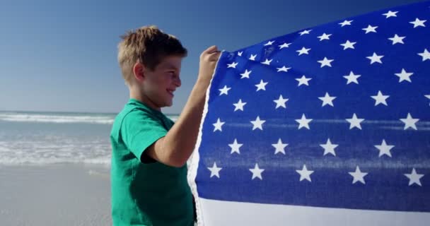 Irmãos segurando bandeira americana na praia — Vídeo de Stock