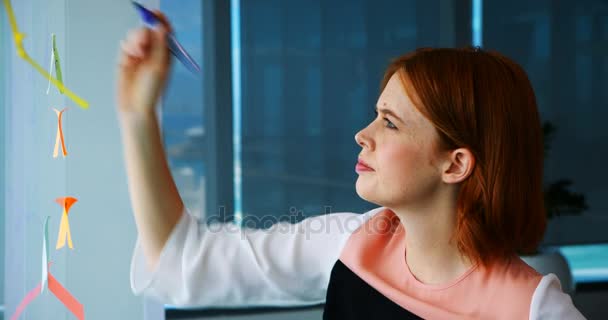 Vrouwelijke uitvoerend schrijven over notitie op glas-bord — Stockvideo