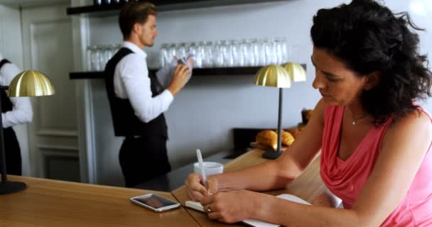 Женщина, пишущая на дневнике у барной стойки — стоковое видео