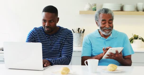 Baba ve oğul mutfakta dizüstü bilgisayar ve dijital tablet kullanarak — Stok video