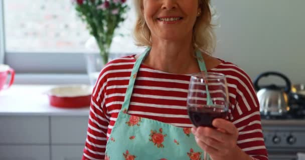 Portrait de femme souriante montrant un verre de vin rouge dans la cuisine — Video