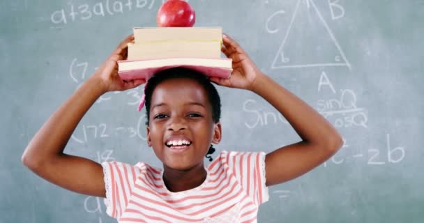 Colegiala sosteniendo libros pila con manzana en la cabeza — Vídeo de stock