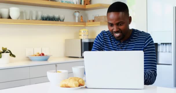 Uomo che utilizza il computer portatile mentre prende il caffè in cucina — Video Stock