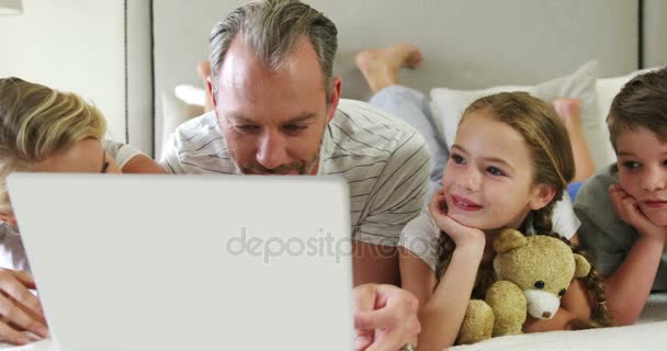 Famille utilisant un ordinateur portable tout en étant couché ensemble dans la chambre à coucher à la maison 4k — Video