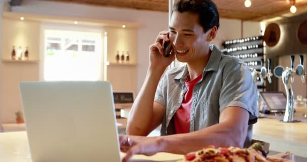 Homme utilisant un ordinateur portable tout en parlant sur un téléphone mobile — Video