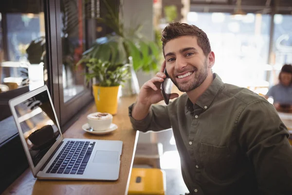 Man talking smartphone while sitting by laptop — Stock Photo, Image