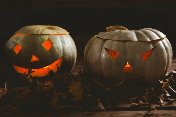 Close up of illuminated kack o lanterns with autumn leaves — Stock Photo, Image