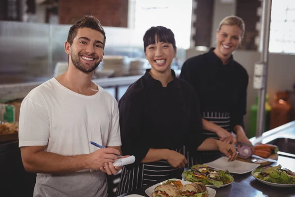 Официант с женскими поварами, стоящими на кухне — стоковое фото