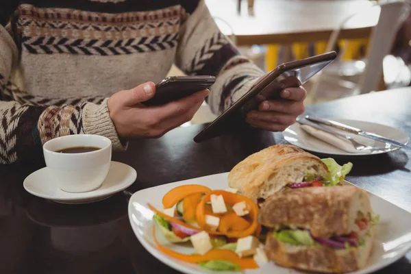 Homem com café da manhã usando telefone e tablet — Fotografia de Stock