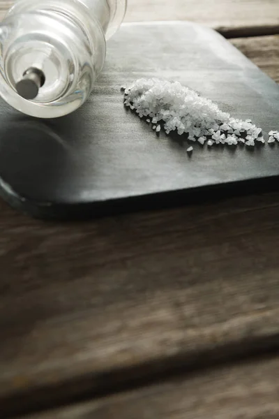 Соляной шейкер и соль на черной пластине — стоковое фото