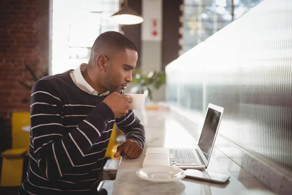 Homem bebendo café enquanto olha para laptop — Fotografia de Stock