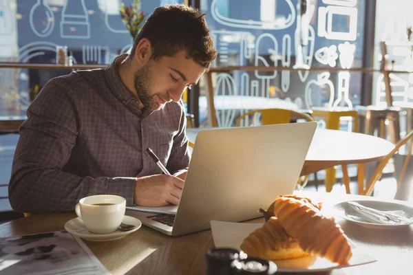 Businessman with laptop writing on paper — Stock Photo, Image