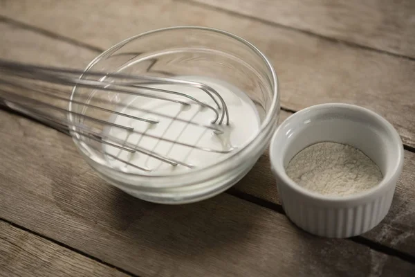 Milk with wire whisk and flour in container — Stock Photo, Image