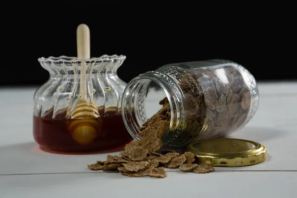 Frasco de mel e flocos de trigo a sair da garrafa — Fotografia de Stock