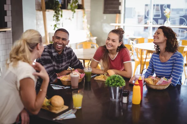 Vrienden praten zittend aan tafel met voedsel — Stockfoto