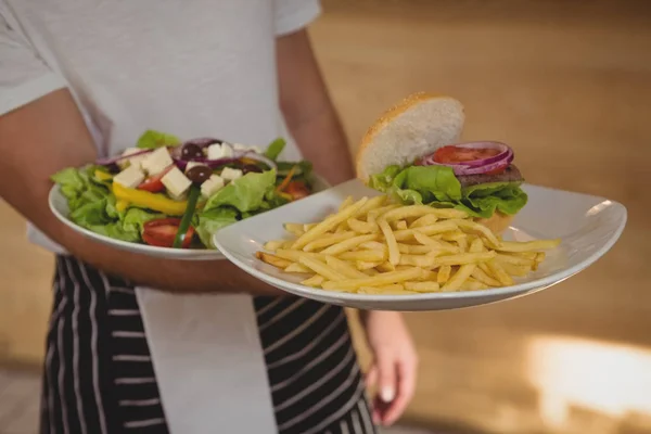 Garçom segurando pratos com batatas fritas e salada — Fotografia de Stock