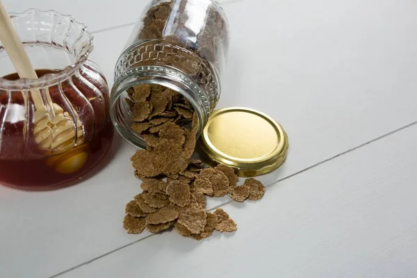 Tarro de miel y copos de trigo derramado de la botella —  Fotos de Stock