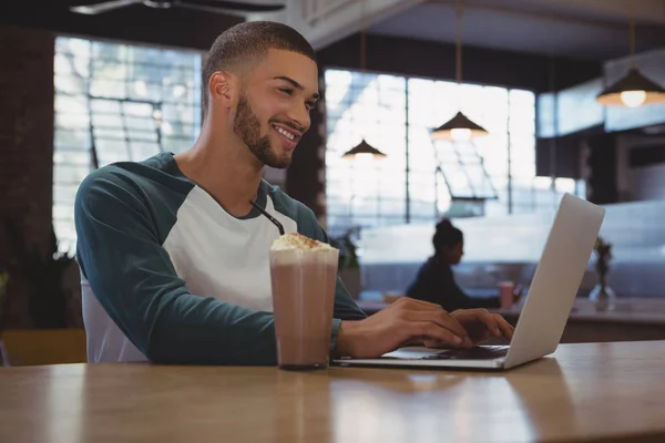 Man met milkshake glazen met behulp van laptop — Stockfoto