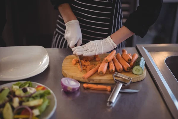 Chef feminino cortando cenouras a bordo na cozinha — Fotografia de Stock