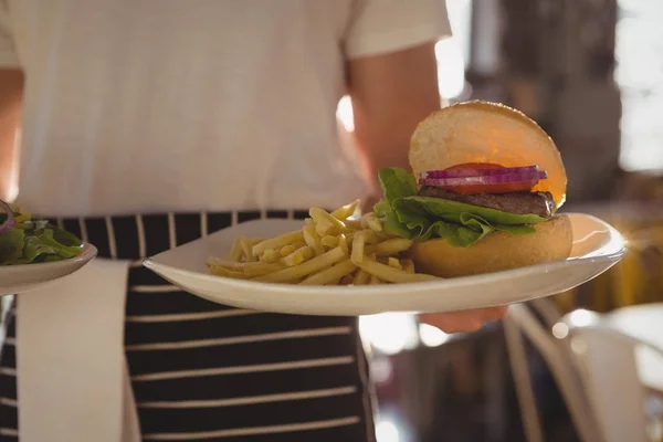 Kellner hält Teller mit Burger und Pommes — Stockfoto