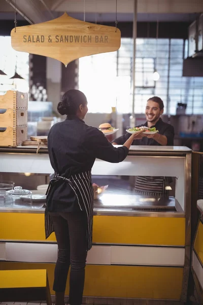 Servitris tar mat tallrikar från servitör på counter — Stockfoto