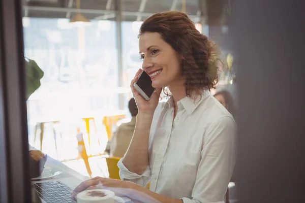 Vrouw met behulp van de laptop tijdens het gesprek op de telefoon — Stockfoto