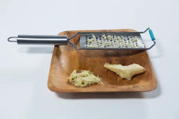 Steel grater and fresh ginger on wooden plate — Stock Photo, Image
