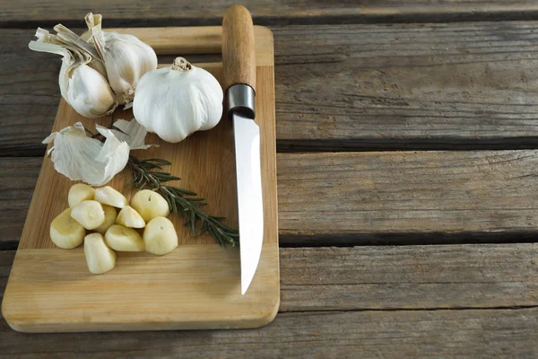Garlic, rosemary and knife on chopping board — Stock Photo, Image
