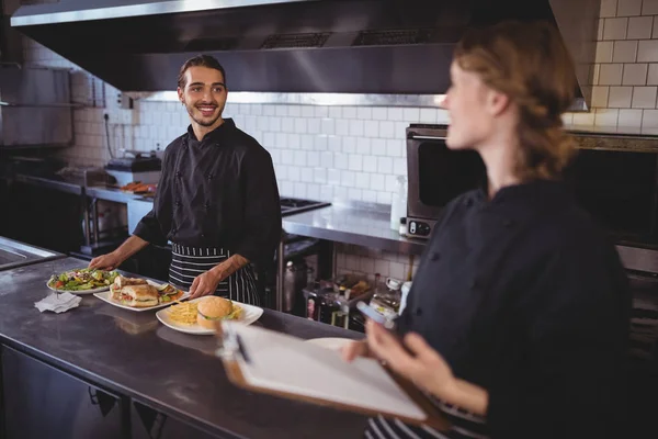 Kellner bereitet Essen zu, während er Kellnerin ansieht — Stockfoto