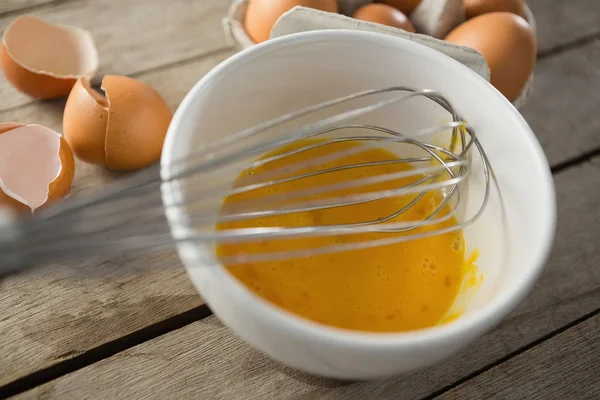 Egg in bowl with wire whisk by eggshells — Stock Photo, Image