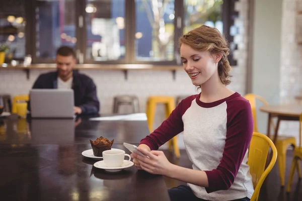 Nainen käyttää älypuhelinta kahvilassa — kuvapankkivalokuva