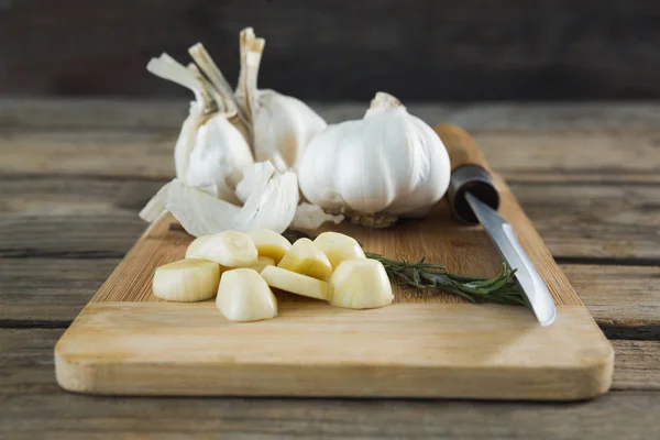 Garlics, rosemary and knife on chopping board — Stock Photo, Image