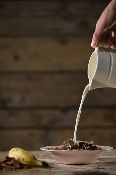Hand gießt Milch auf Weizenflocken — Stockfoto