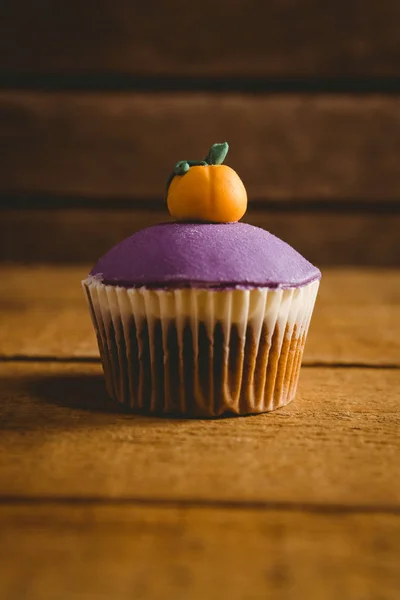 Purple cup cake with pumpkin icing on wooden table — Stock Photo, Image