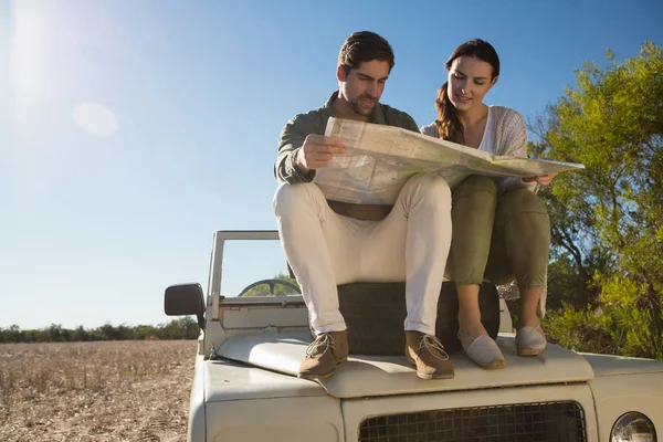 Pareja sosteniendo mapa en neumático sobre vehículo todoterreno — Foto de Stock