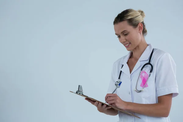Γιατρός με ροζ κορδέλα γράφοντας στο Πρόχειρο — Φωτογραφία Αρχείου